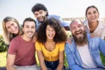 Multiracial group of young people - Happy millennial friends from different cultures smiling at smartphone camera - Friendship and youth concept with diverse millennial students sitting together