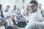 Group of young adults sitting around talking with man in glasses turned and smiling