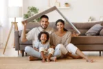 cheerful-parents-with-child-smiling-and-keeping-roof-mockup-over-heads-while-sitting-on-floor-in-cozy-living-room-during-relocation-stockpack-istock Cheerful parents with child smiling and keeping roof mockup over heads while sitting on floor in cozy living room during relocation