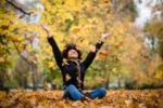 Happy woman in autumn park drop up leaves