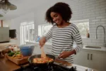 Woman mixing ingredients and vegetables in pan while preparing lunch indoors