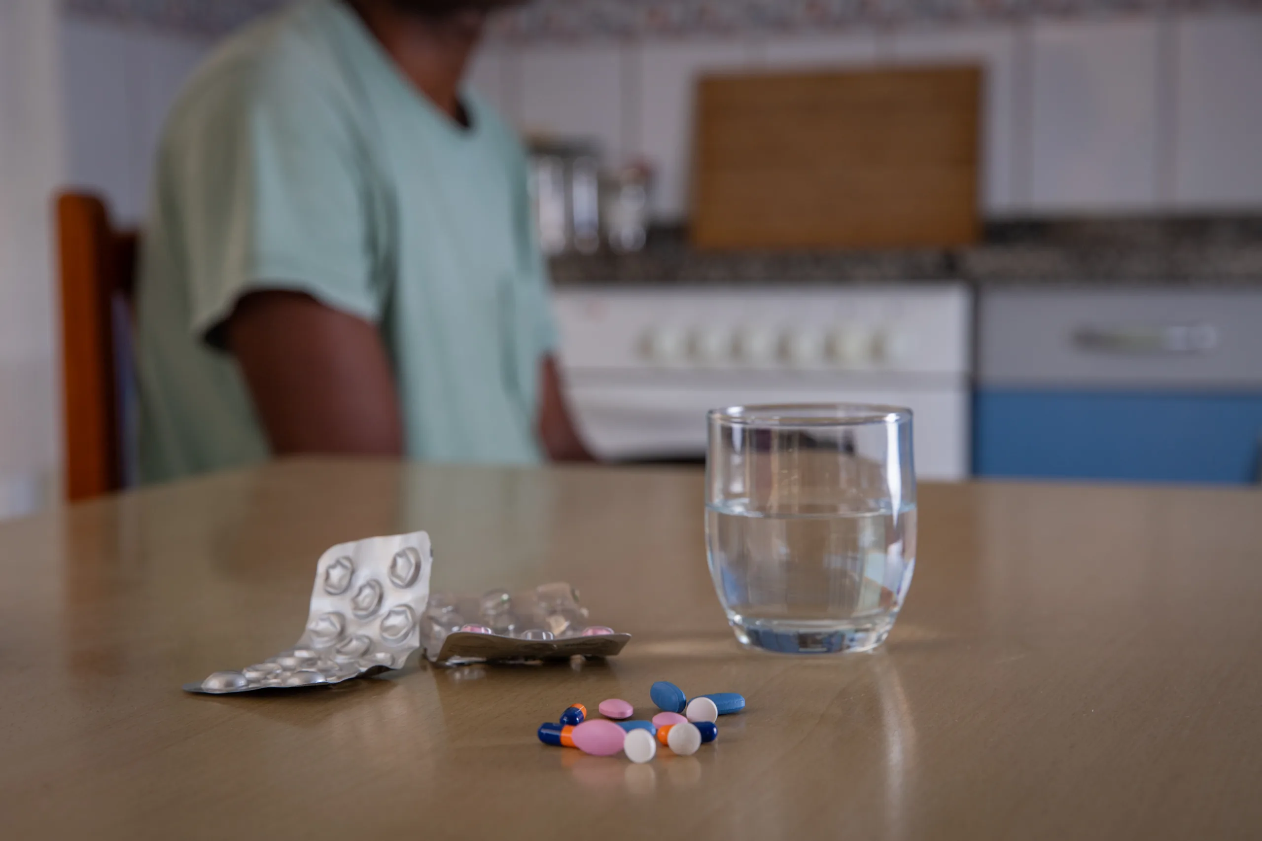 Close up of some medicines and a glass of water, person sitting behind, concept of drug consumption