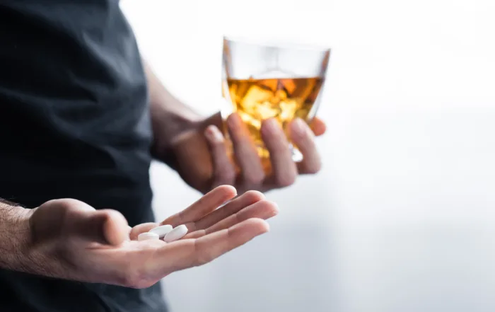 partial view of depressed man with glass of whiskey and handful of pills