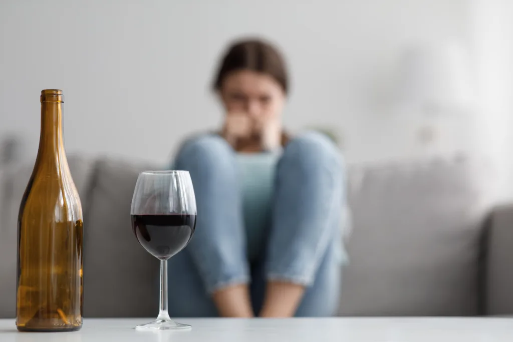 Young woman sitting on couch looking at bottle and glass of wine