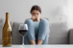 Young woman sitting on couch looking at bottle and glass of wine