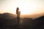 Woman meditating at sunset in the mountains practicing her spirituality