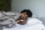 Young black woman laying in bed experiencing hangxiety after consuming too much alcohol the night prior