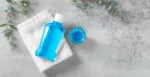 Mouthwash on white towel with cup and eucalyptus on grey table, flatlay, oral care background with copy space