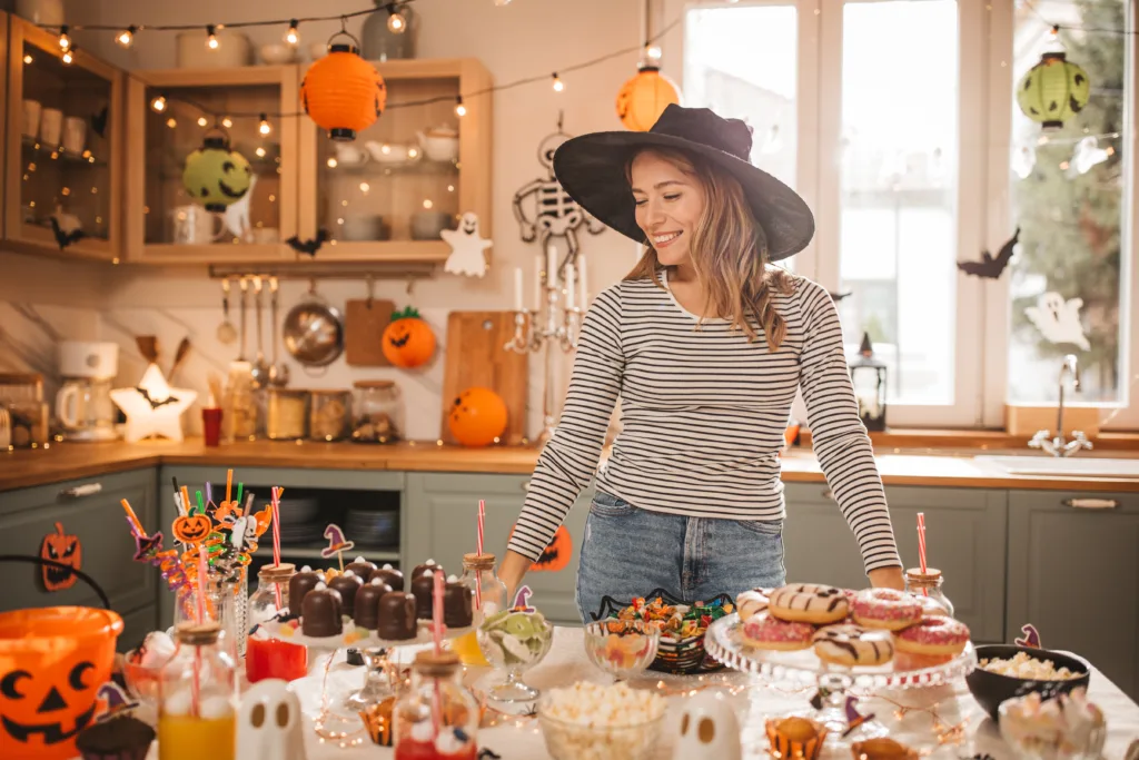 Young woman in costume setting sweet table for Halloween lunch.