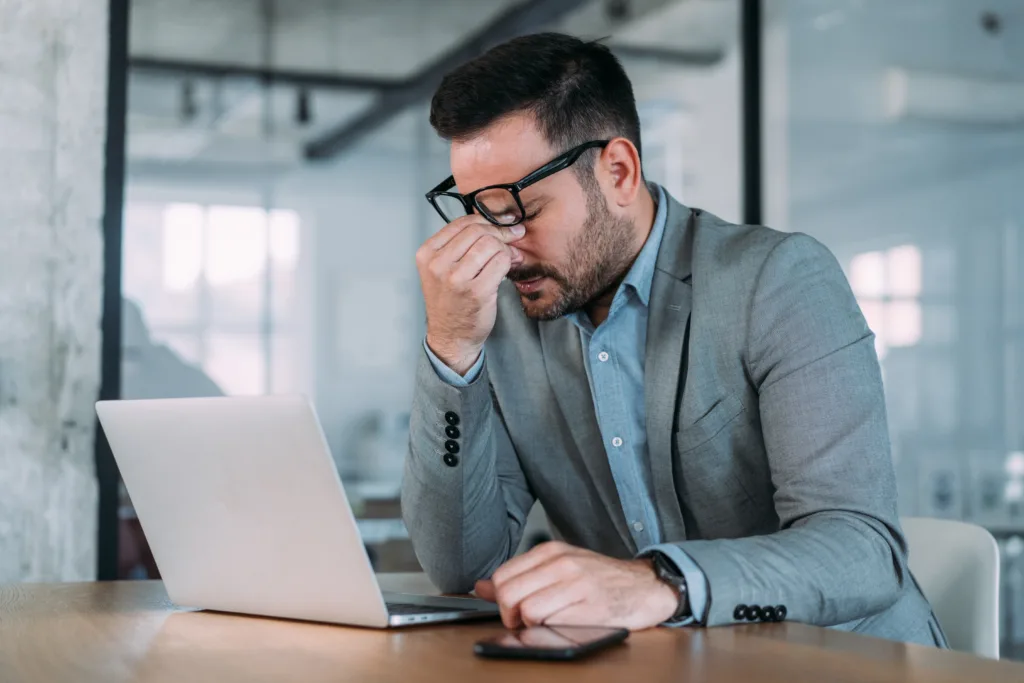 Shot of stressed businessman sitting at his desk and holding head with hand. Overworked businessman sitting in front of laptop and holding head.