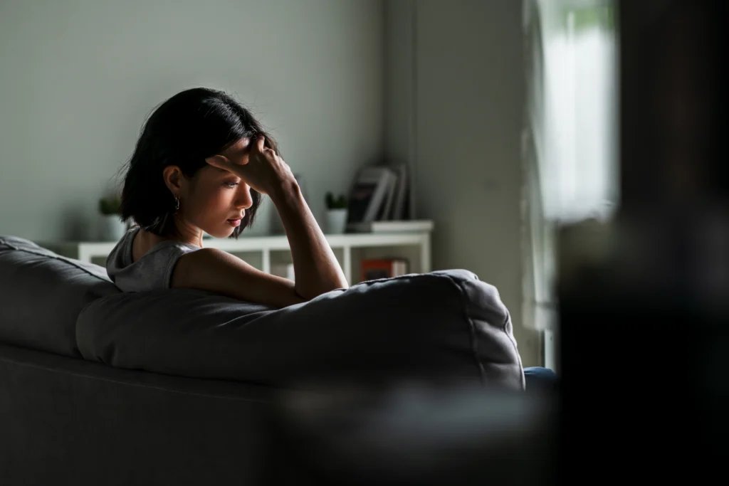 Young woman sitting on sofa at home feeling sad tired and worried suffering depression in mental health.