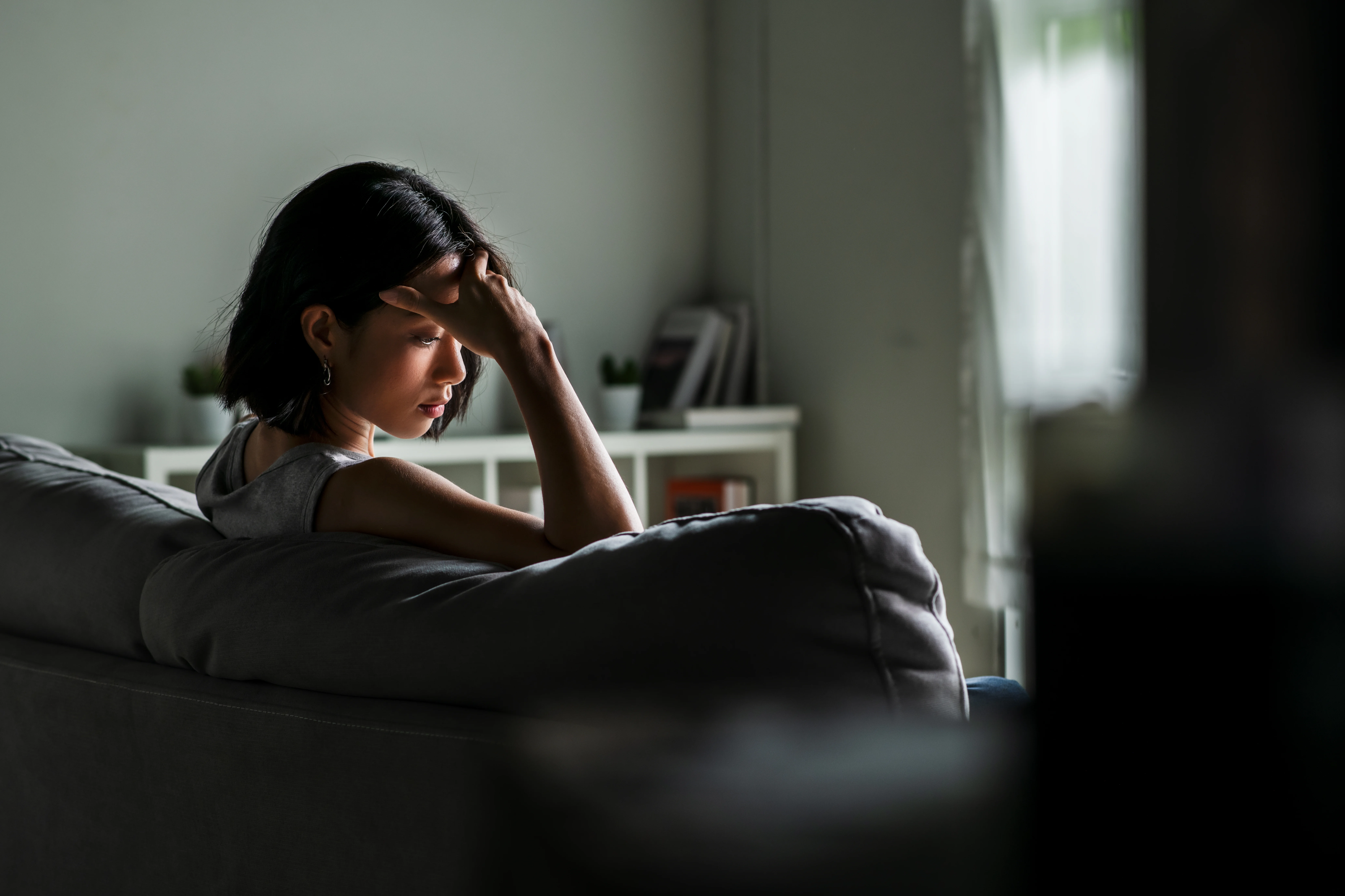 Young woman sitting on sofa at home feeling sad tired and worried suffering depression in mental health.