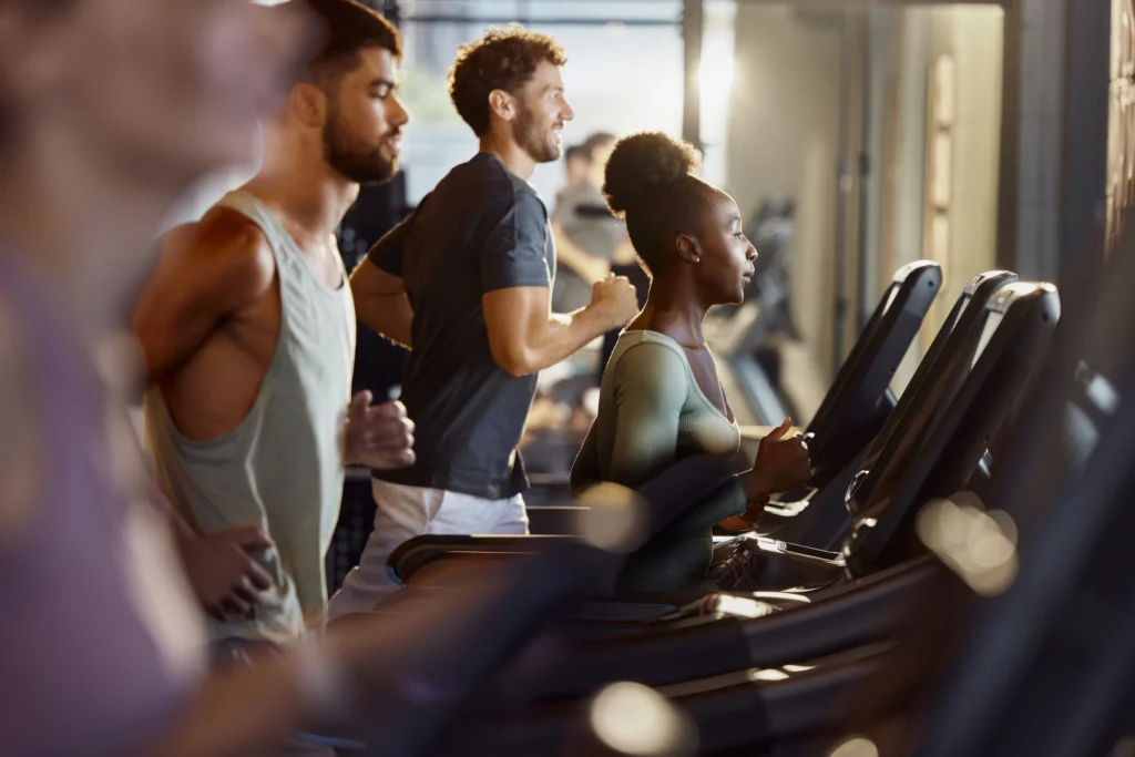 Female athlete jogging during sports training on treadmill among other athletes in a gym.