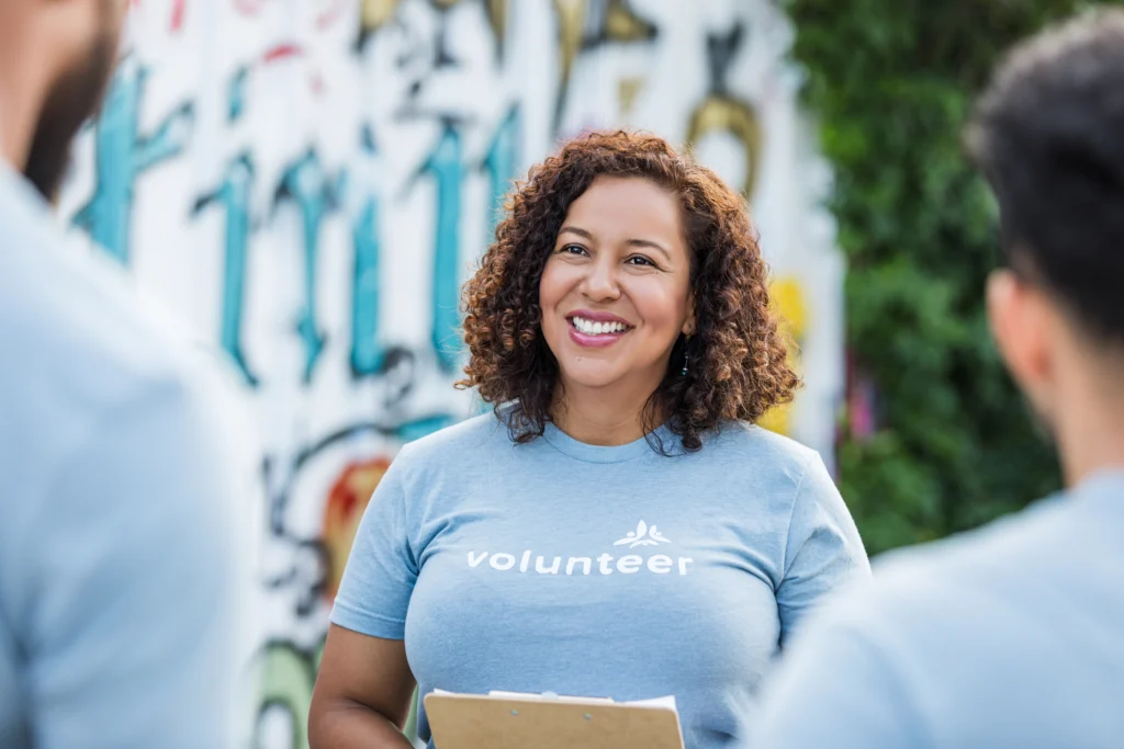 Happy woman in volunteer shirt talking to people outdoors.  Community event.