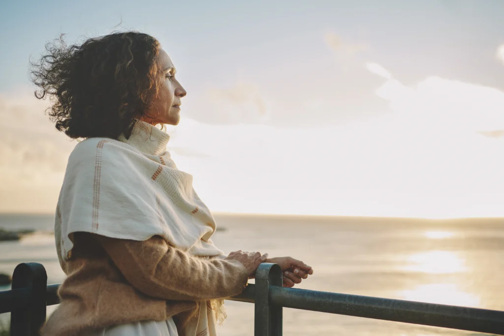 Woman wearing a pashmina leaning on a railing and looking out at the sunset over the ocean
